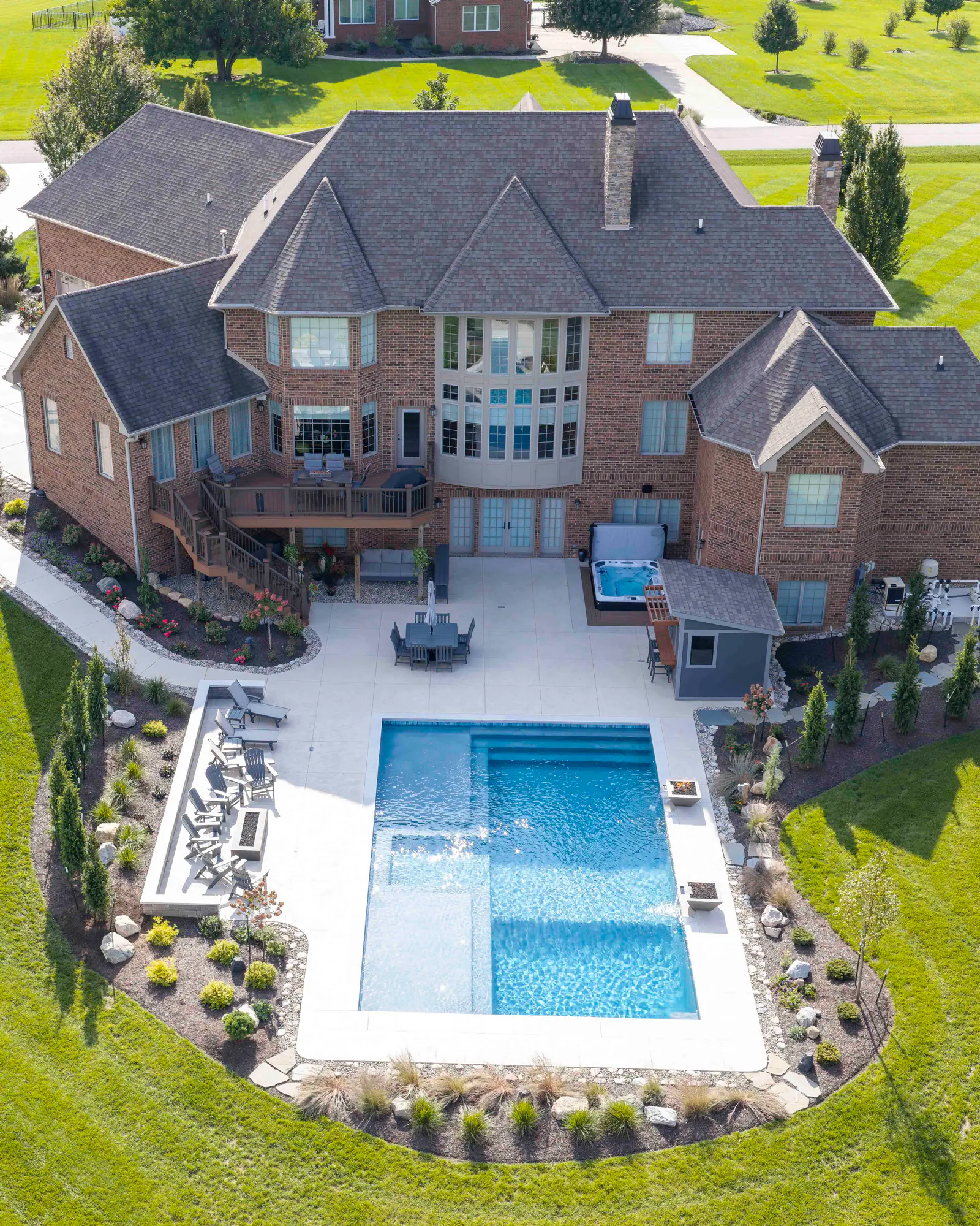 Aerial view of a brick home, its deck, and a rectangular backyard pool