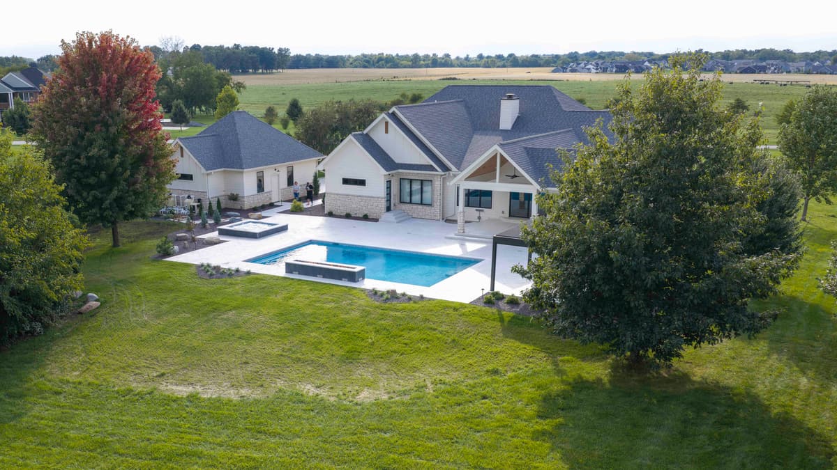 Lawn-level view across the yard to a white home with a rectangular pool and raised spa