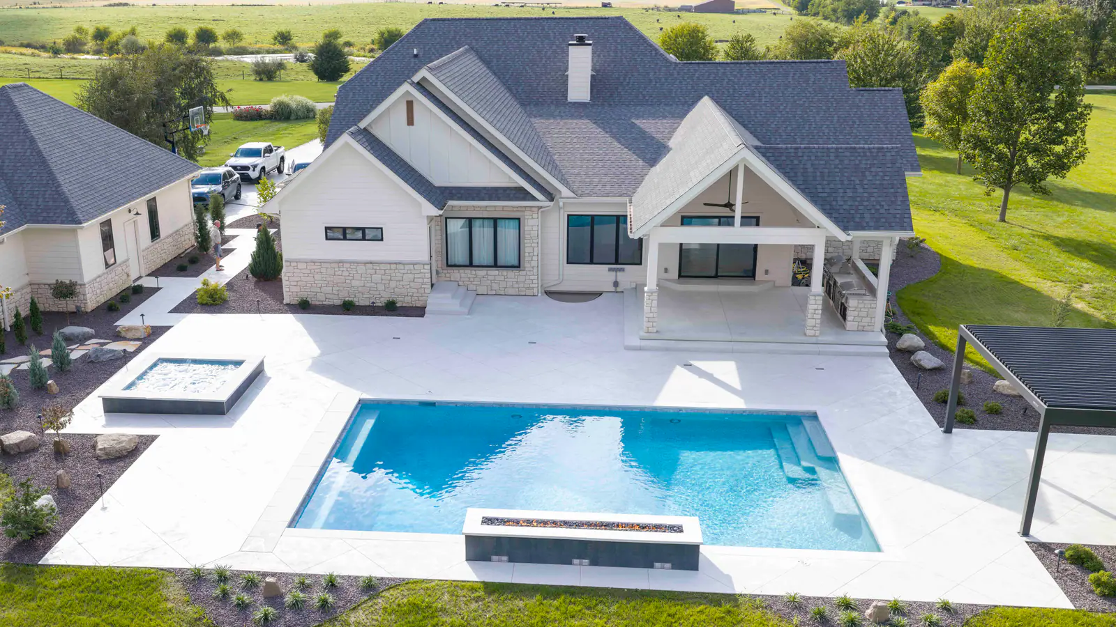 Gunite pool and spa framed by a white paver patio and the covered porch of a modern farmhouse