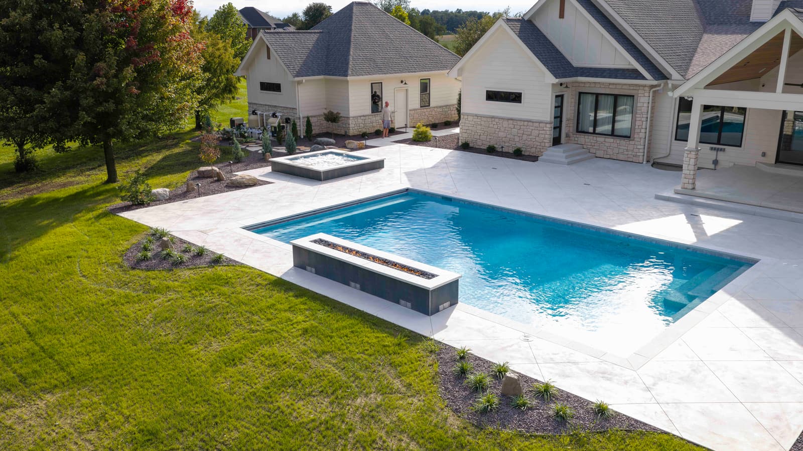 Low aerial view of a gunite pool with a raised linear feature along the water’s edge and a raised spa behind