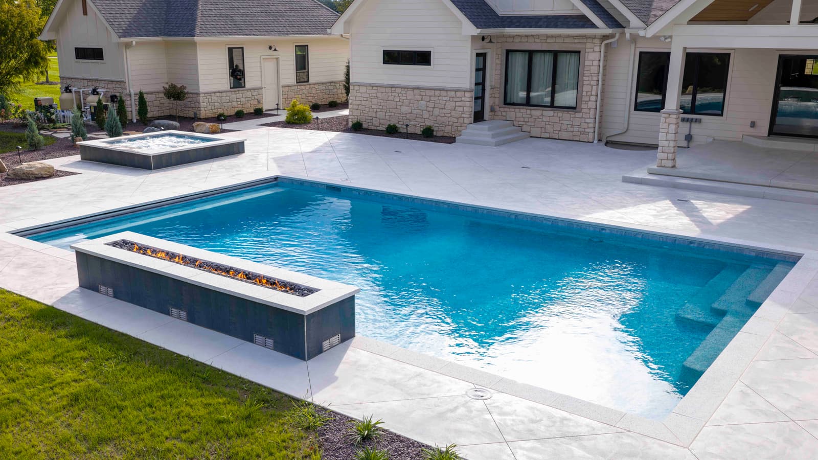 Gunite pool with a raised linear feature, raised spa, and entry steps beside a modern farmhouse patio