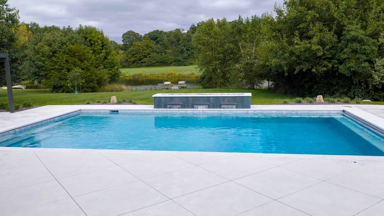 Patio-level view across a blue gunite pool toward a raised spa and a tree line
