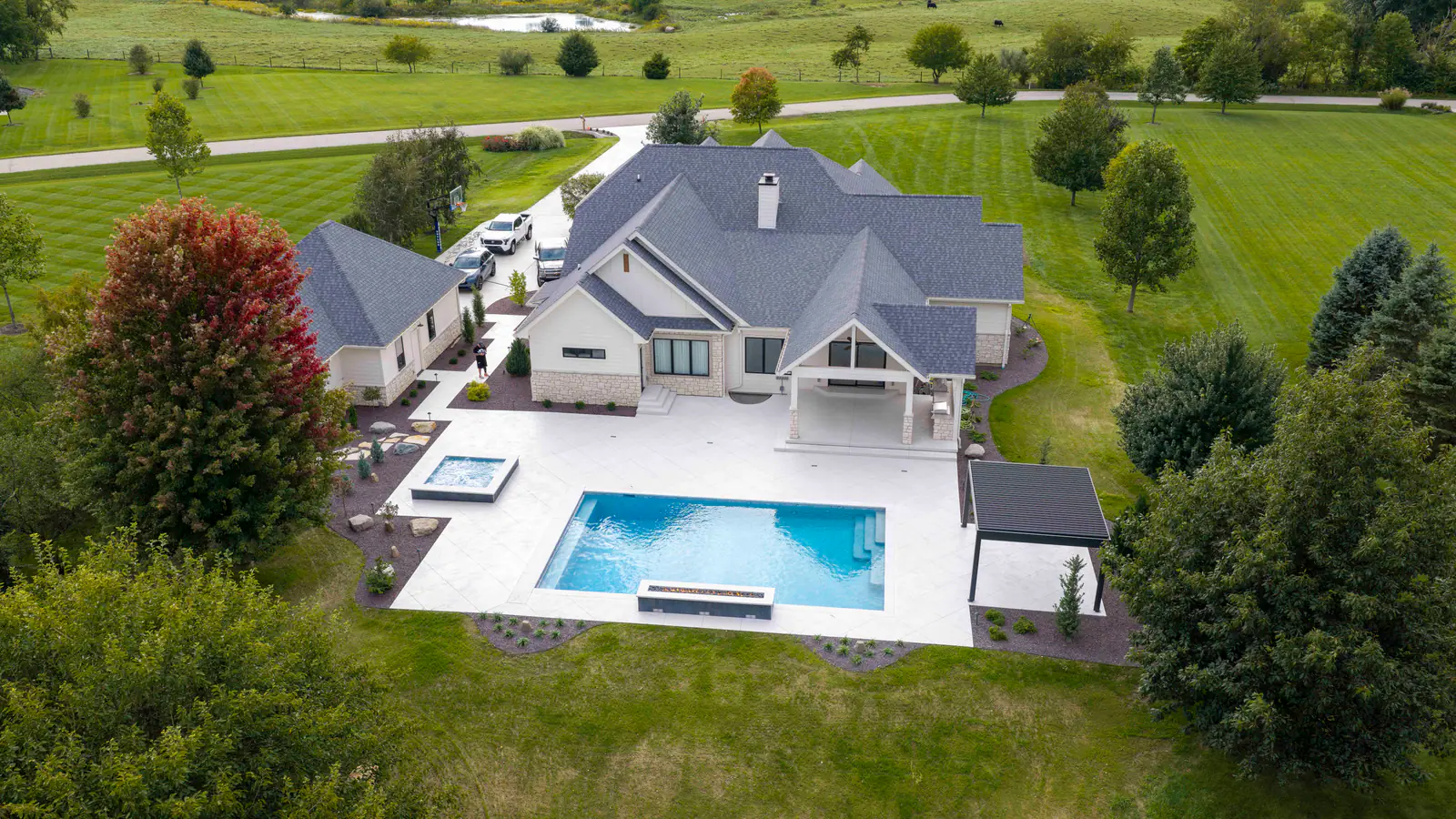Aerial view of a white home with a rectangular backyard pool, raised spa, pergola, and wide paver patio