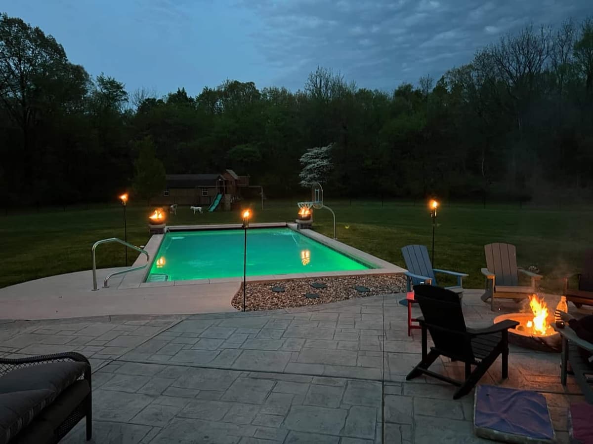 Pool at dusk with tiki torches, Adirondack chairs, and a fire pit
