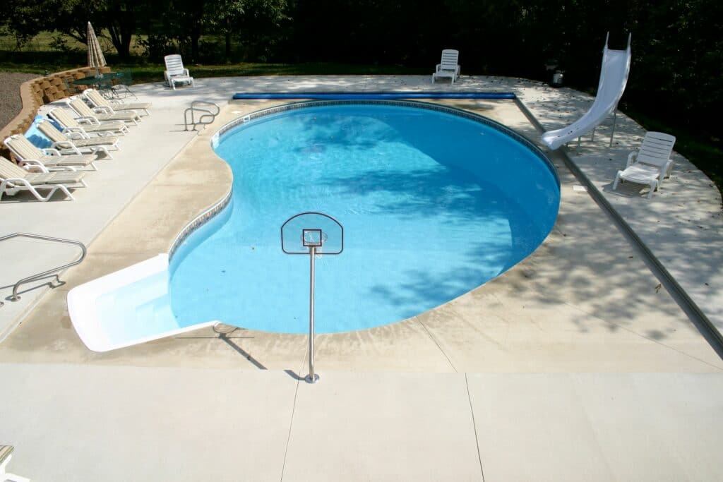 Kidney-shaped pool with a slide, diving board, and basketball hoop