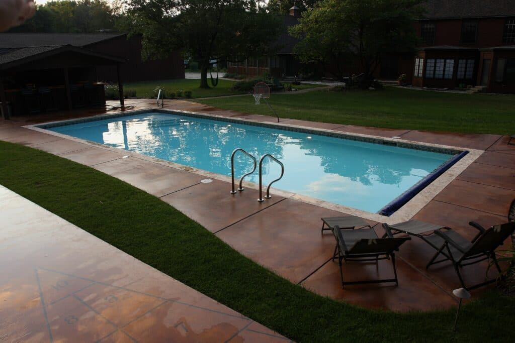 Rectangular pool with a stained concrete deck, ladder, and patio chairs