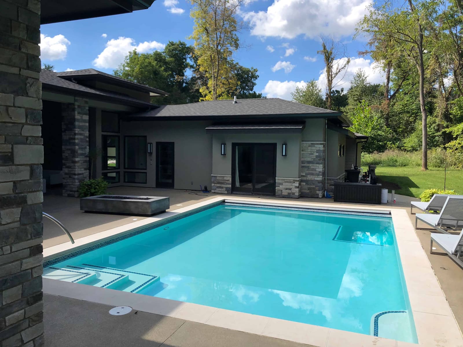 Rectangular gunite pool with tiled steps behind a modern stone home