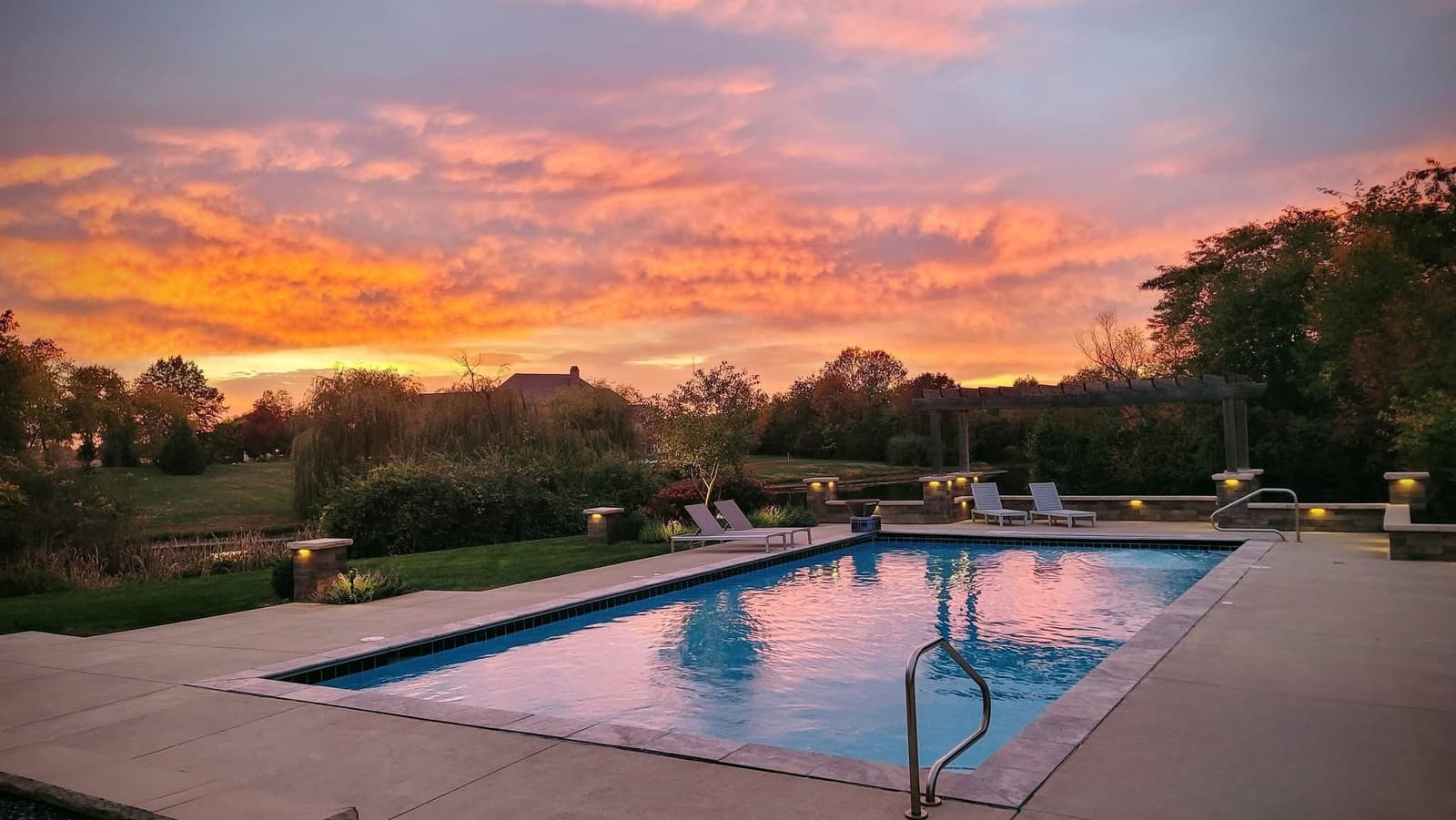Backyard pool reflecting an orange and violet sunset sky