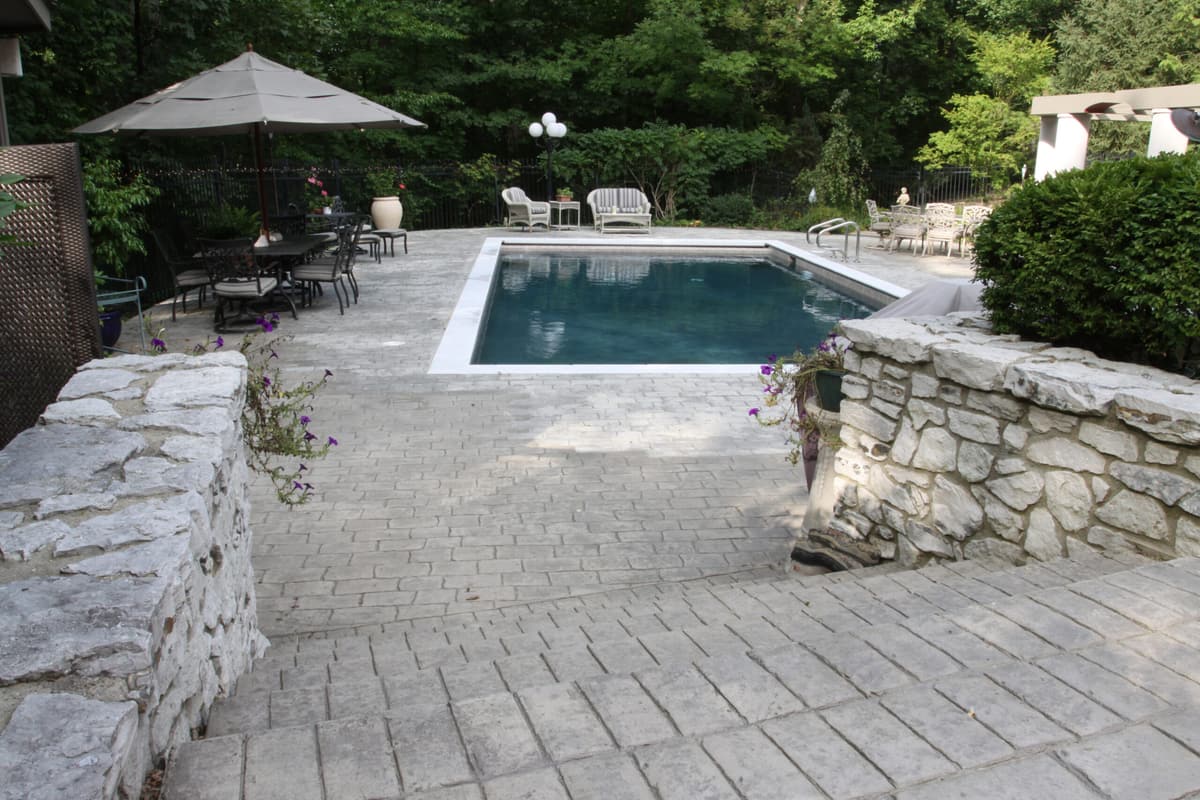 Stacked natural stone walls framing a paver patio and rectangular pool