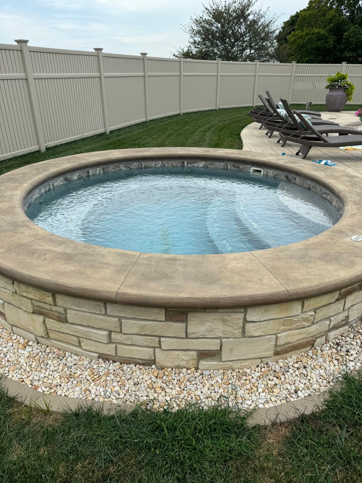 Raised round spa with a stone surround and lounge chairs