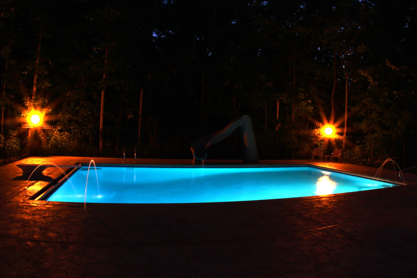 Pool glowing at night beside lit patio lanterns