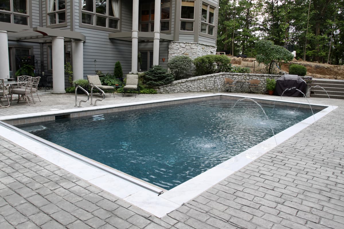 Rectangular pool with a paver deck and deck jets in front of a home