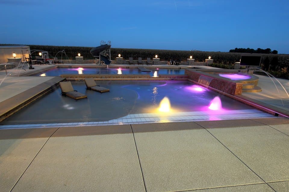 Pool lit with colored LED lights and a tanning ledge at dusk