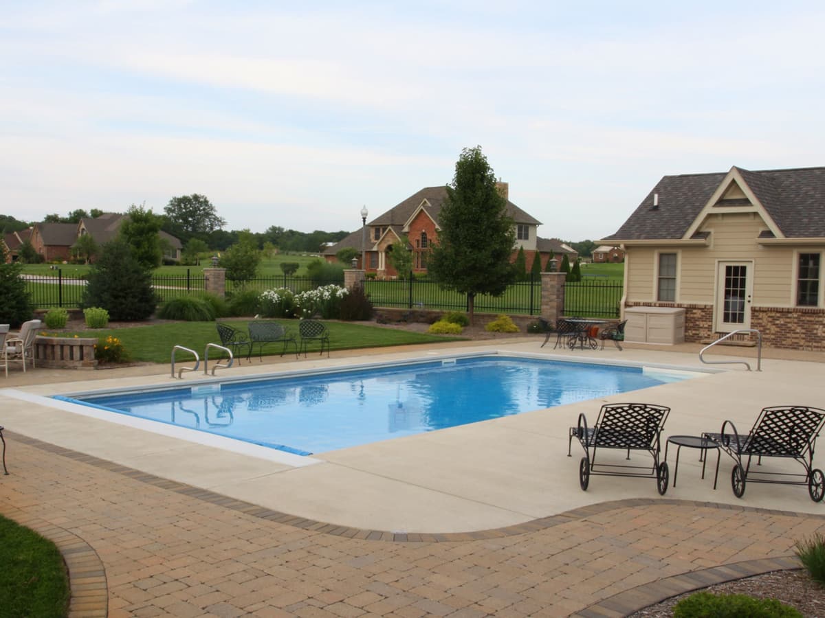 Freeform pool with a paver deck and patio seating beside a pool house