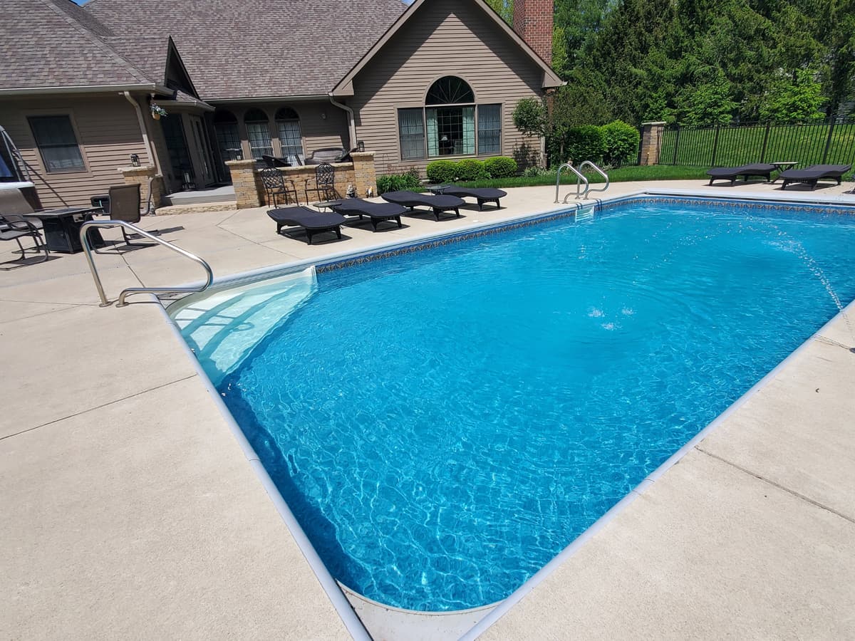 Freeform pool with a waterfall and paver deck behind a stone home