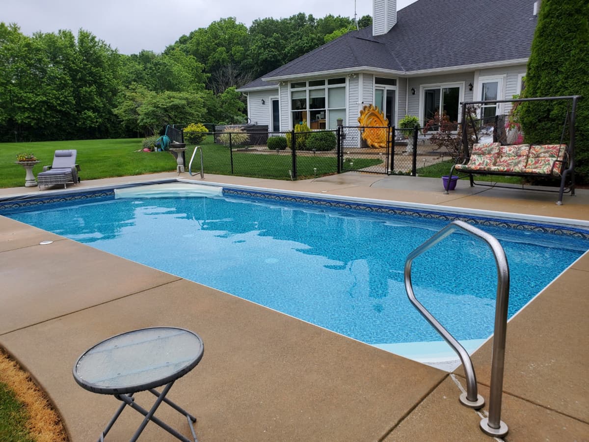 Pool with a handrail and lawn beside a home